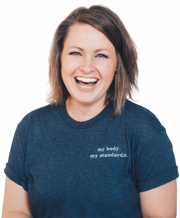 Eine lachende Frau mit schulterlangem braunem Haar trägt ein dunkelblaues T-Shirt. Der Hintergrund ist hell und neutral.